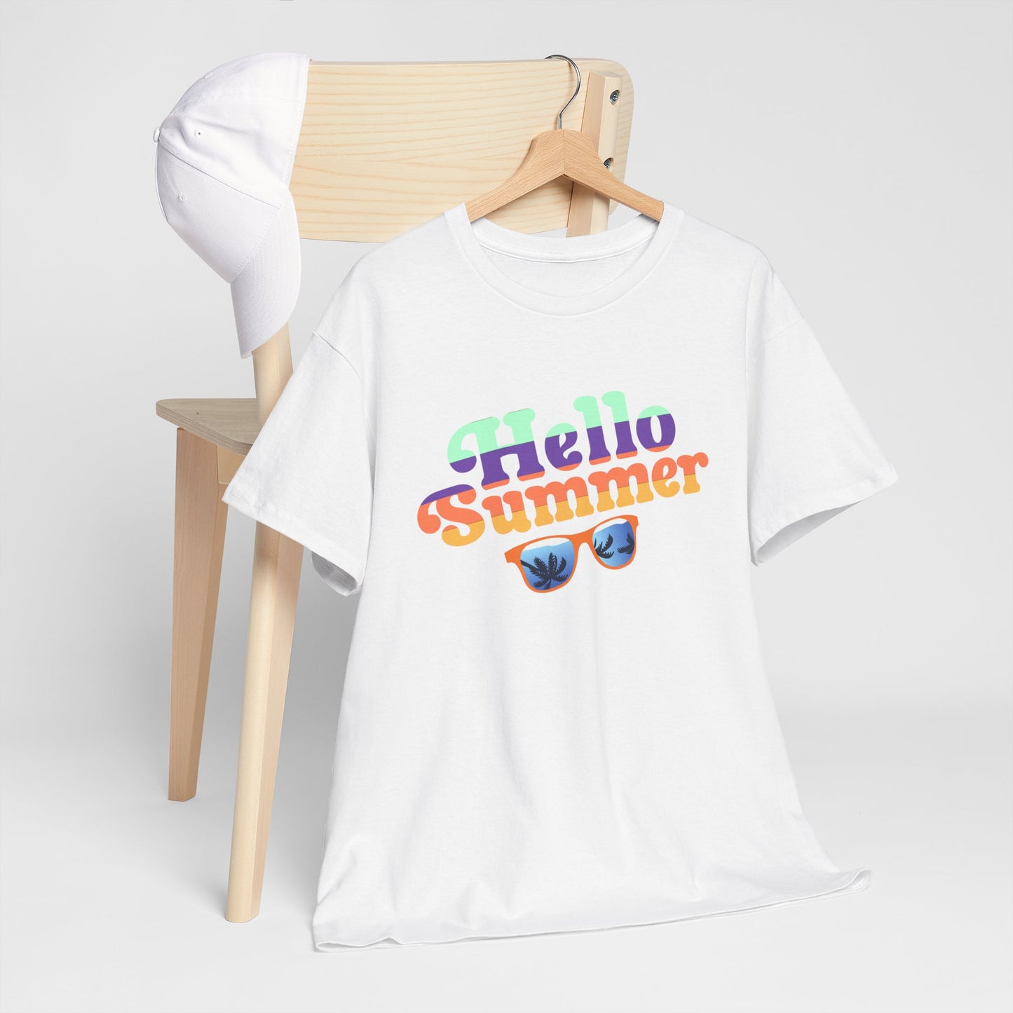 White Printify T-Shirt with Hello Summer colorful summer event shirt design displayed on wooden chair with white cap